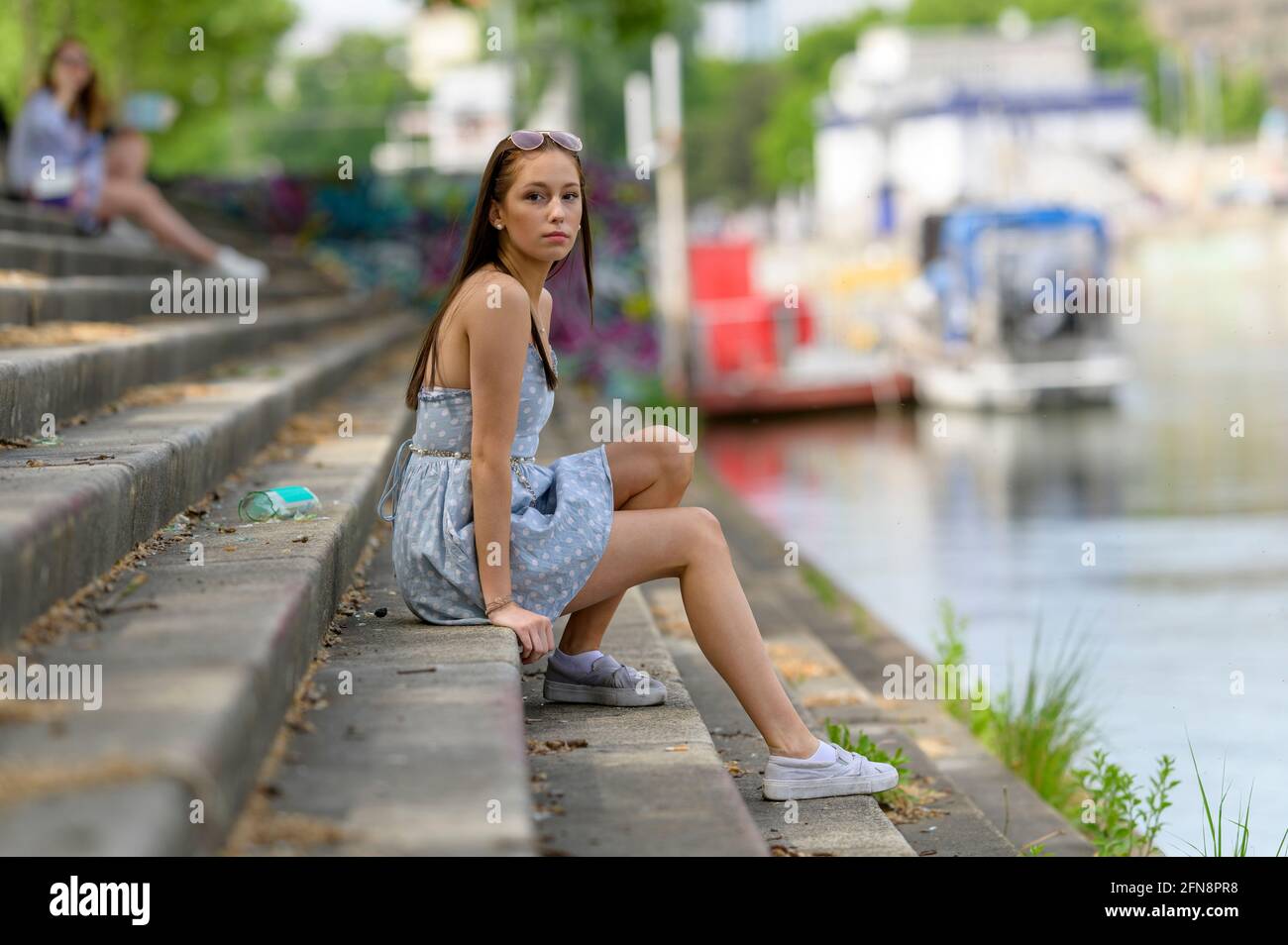 Un ritratto di una bella giovane donna preso in estate in una città seduta su una scala accanto ad un fiume. Foto Stock