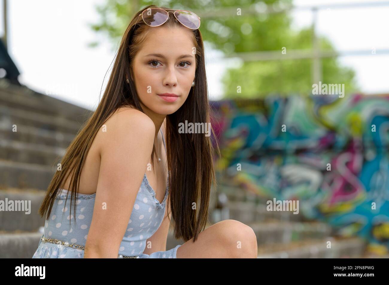Un ritratto di una bella giovane donna preso in estate in una città seduta su una scala accanto ad un fiume. Foto Stock