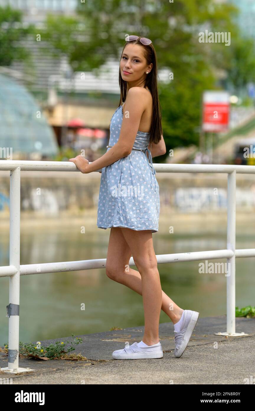 Un ritratto di una donna piuttosto giovane, scattata in estate in una città, appoggiata a una ringhiera su un fiume vicino. Foto Stock
