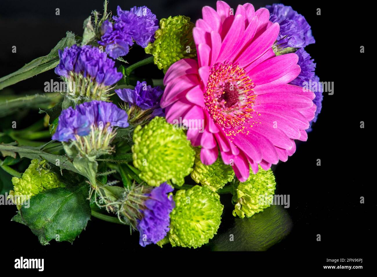 Una bella disposizione di fiori recisi rosa, verde e viola si trova su una superficie nera. Foto Stock