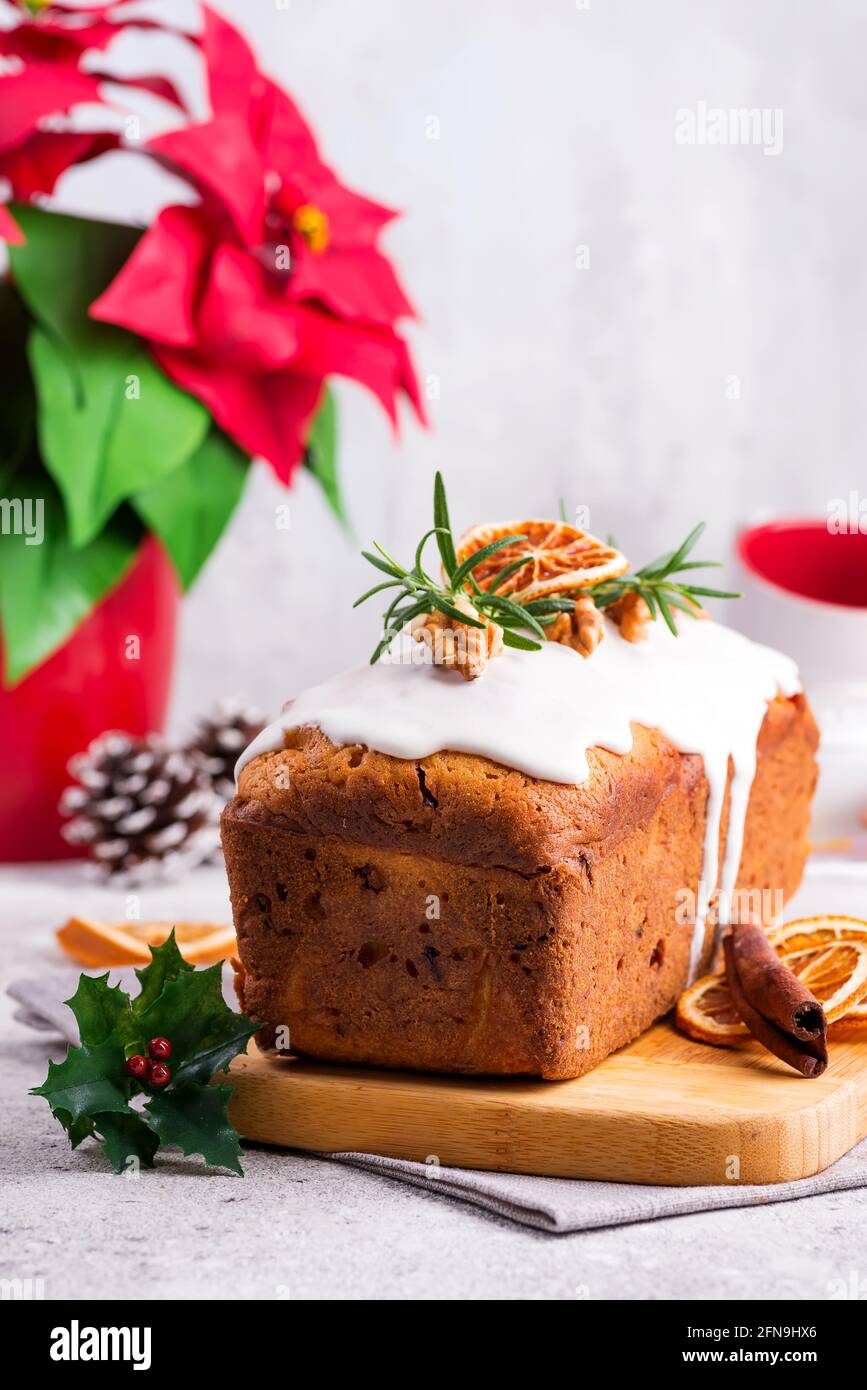 Torta di pane di frutta spolverata con glassa, noci e arancio secco su fondo di pietra. Natale e Vacanze invernali Poinsettia sullo sfondo Foto Stock