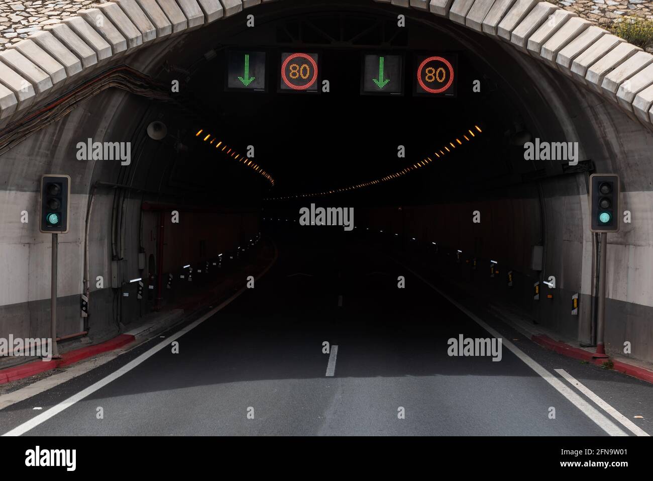 Ingresso ad un tunnel autostradale con due corsie, semafori verdi e cartelli illuminati che indicano la velocità massima a ottanta. Foto Stock