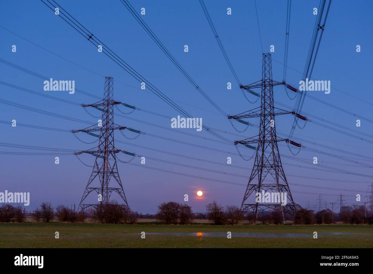 Linee elettriche al tramonto sulle paludi del Tamigi in basso Higham Kent con una luna piena che sale Foto Stock