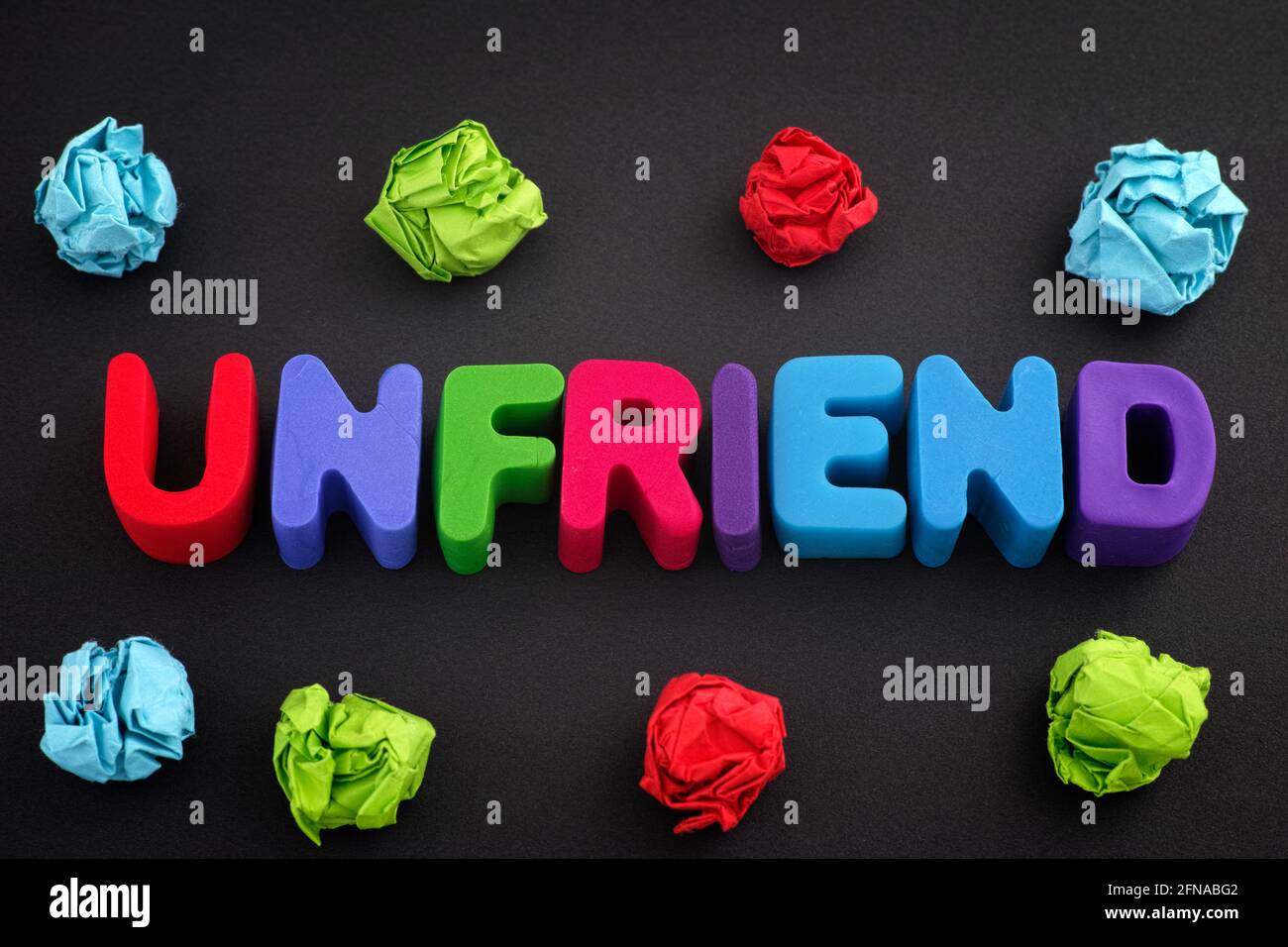 La parola Unfriend fatto di lettere di argilla di polimero con alcune palline di carta sminuzzate colorate intorno ad esso. Primo piano. Foto Stock