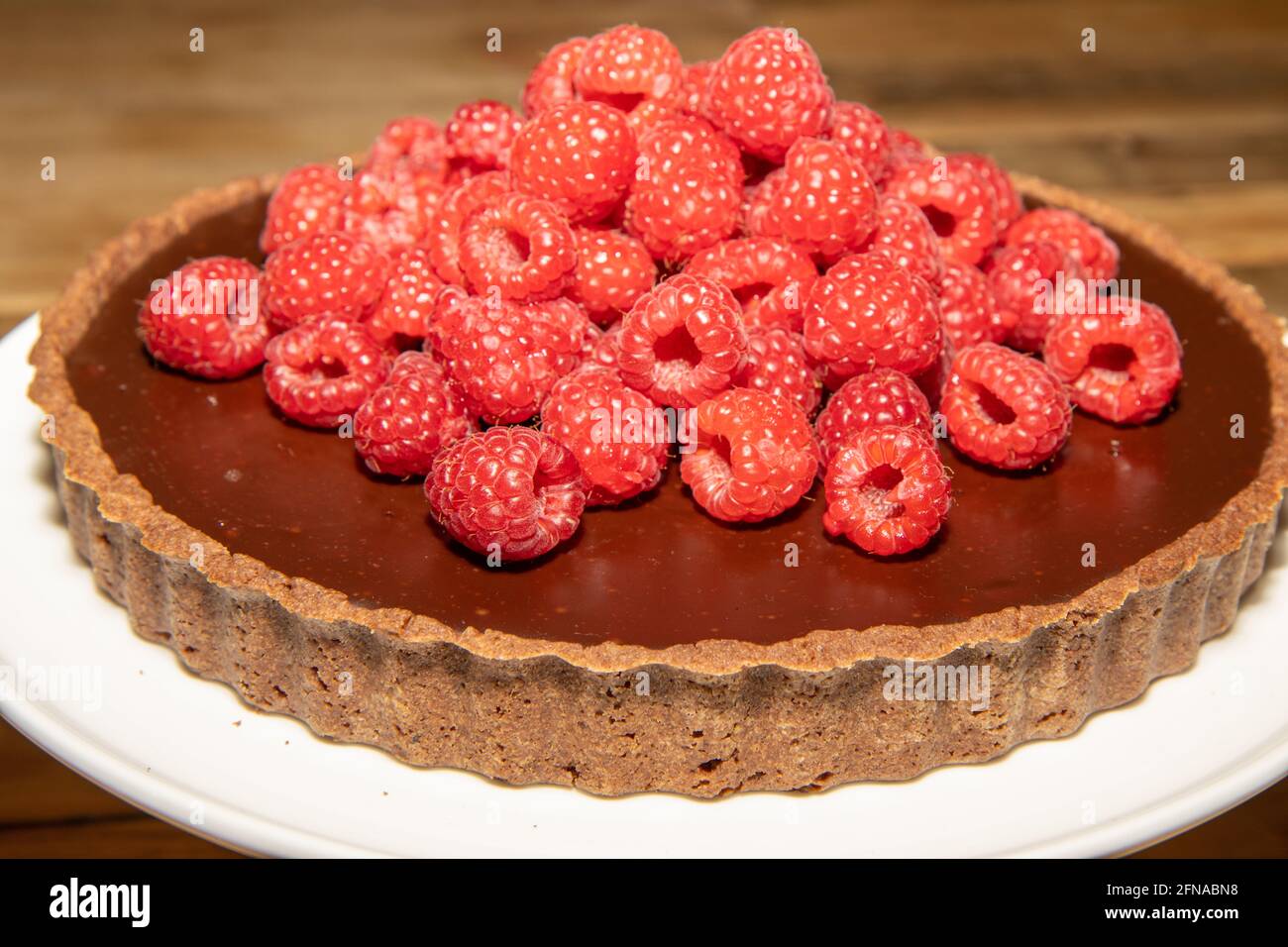 Una deliziosa crostata di cioccolato fondente con lamponi freschi un tavolo da cucina in legno Foto Stock