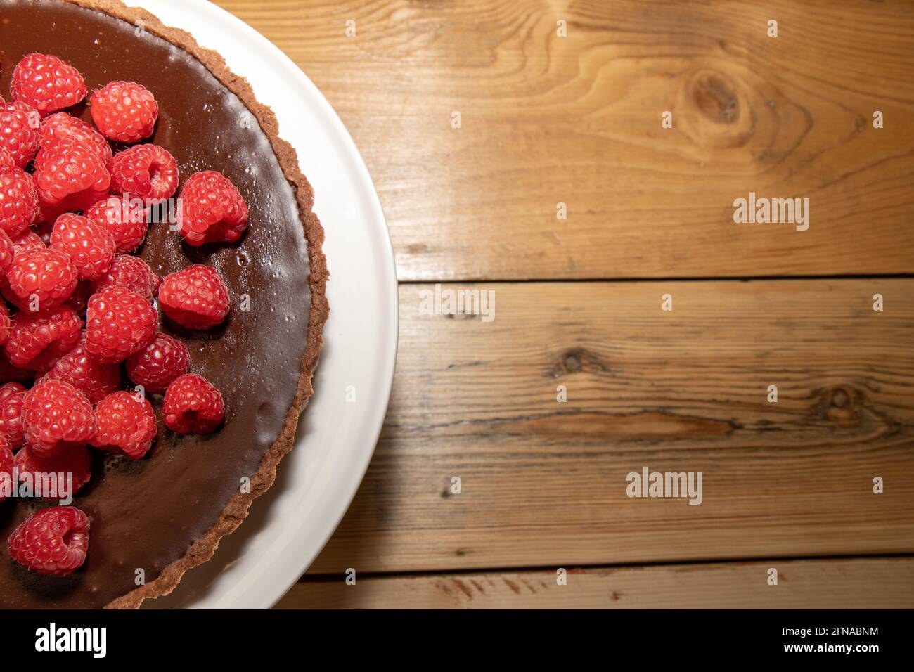 Una deliziosa crostata di cioccolato fondente con lamponi freschi un tavolo da cucina in legno Foto Stock