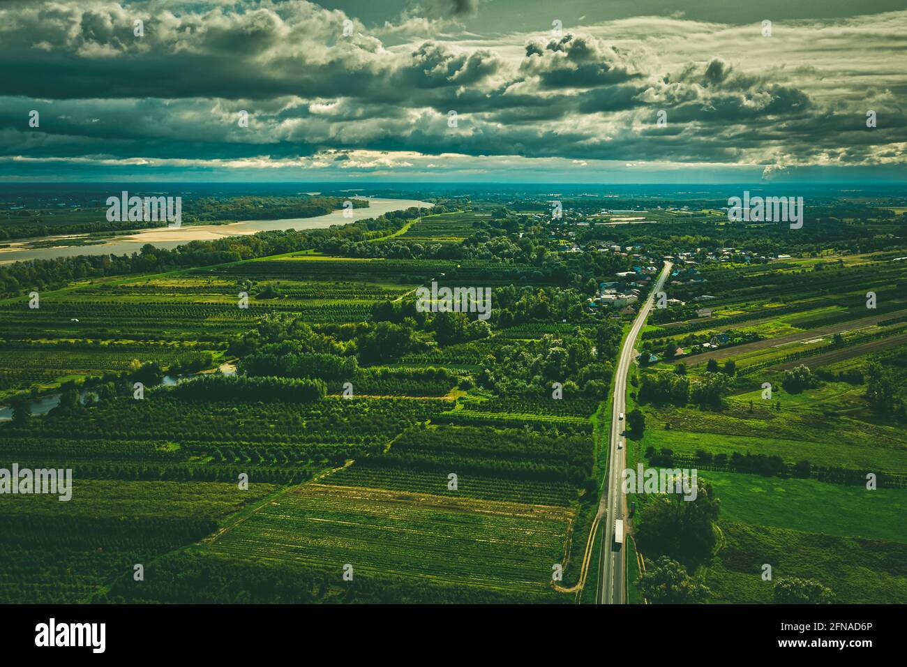 Paesaggio panoramico aereo, villaggio su strada diritta e fiume lontano sotto cielo nuvoloso moody Foto Stock