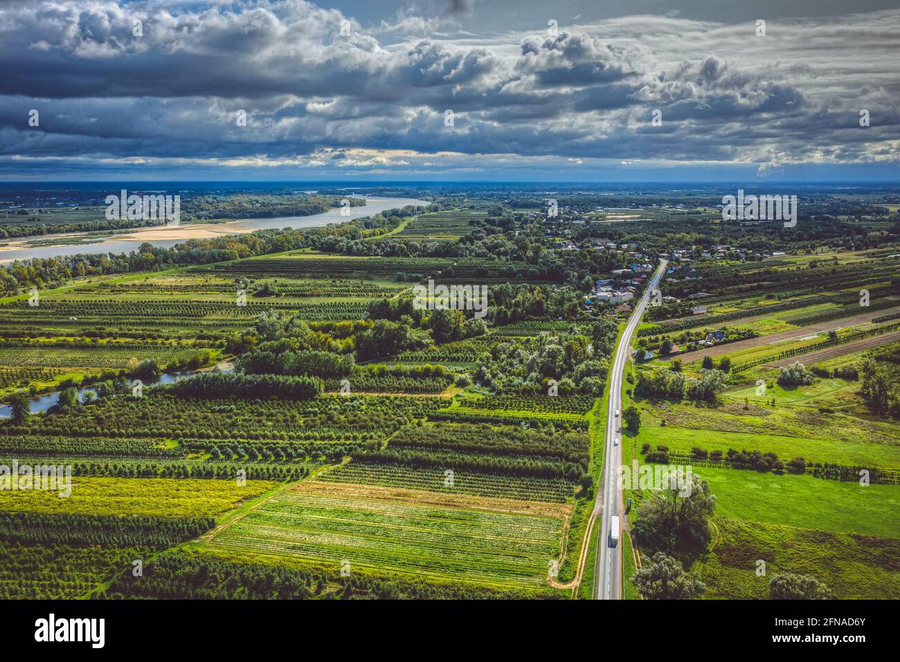 Paesaggio panoramico aereo, villaggio su strada diritta e fiume lontano sotto cielo nuvoloso moody Foto Stock