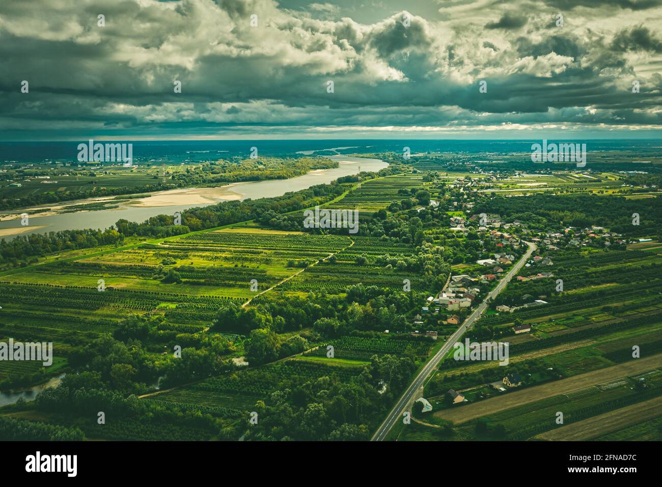 Paesaggio panoramico aereo, villaggio su strada diritta e fiume lontano sotto cielo nuvoloso moody Foto Stock