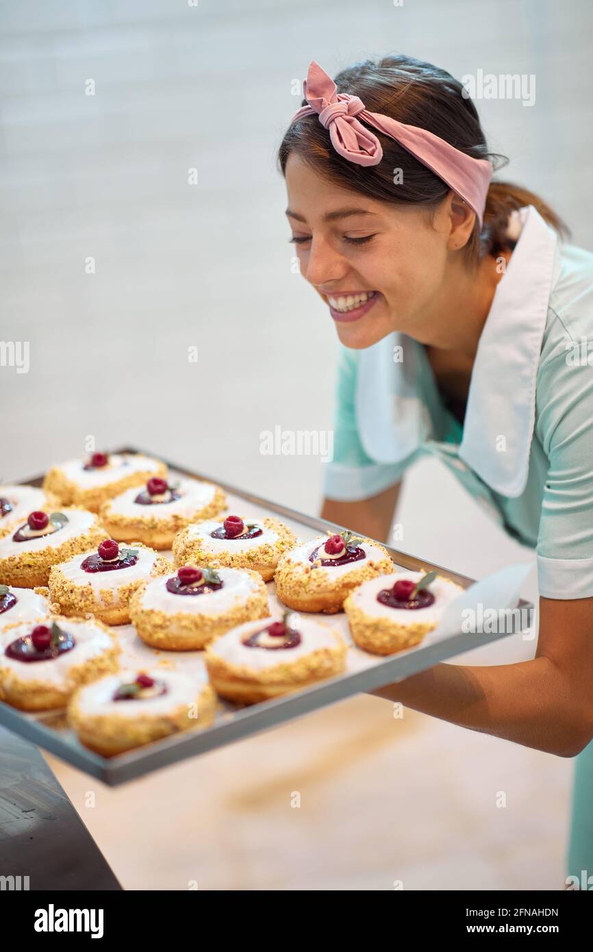 Una giovane donna di piccola impresa è pasionatly guardando le sue deliziose ciambelle fatte a mano di aspetto irresistibile. Pasticceria, dessert, dolce, fare Foto Stock