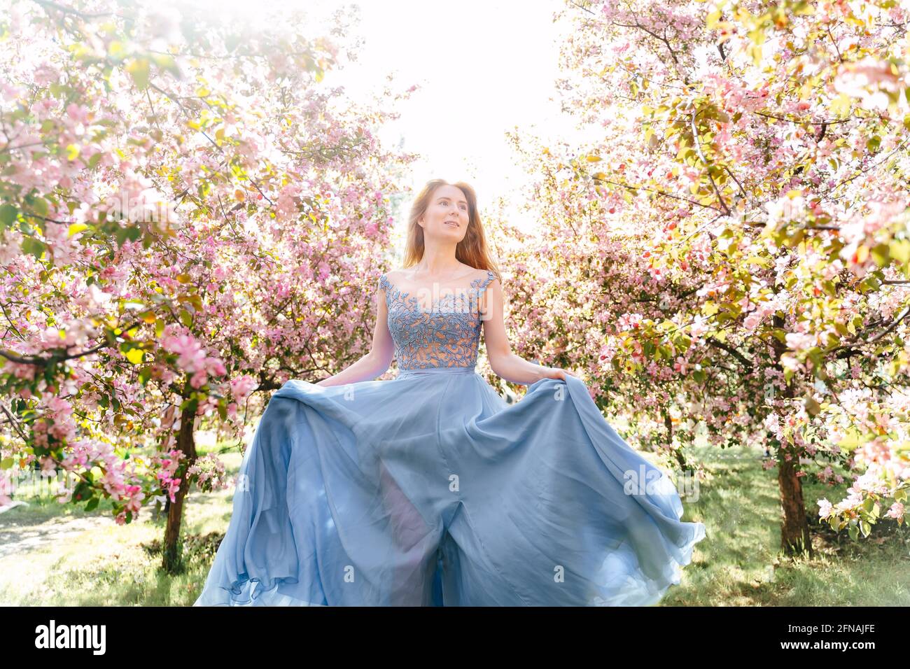 Una ragazza in un vestito blu che scorre cammina attraverso un giardino fiorito rosa. Foto Stock