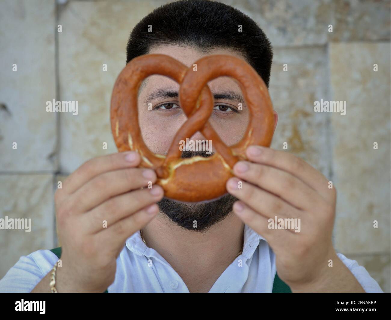 Bel giovane panettiere caucasico tiene un tradizionale pretzel bavarese con entrambe le mani e guarda attraverso il cappio pretzel al pretzel. Foto Stock