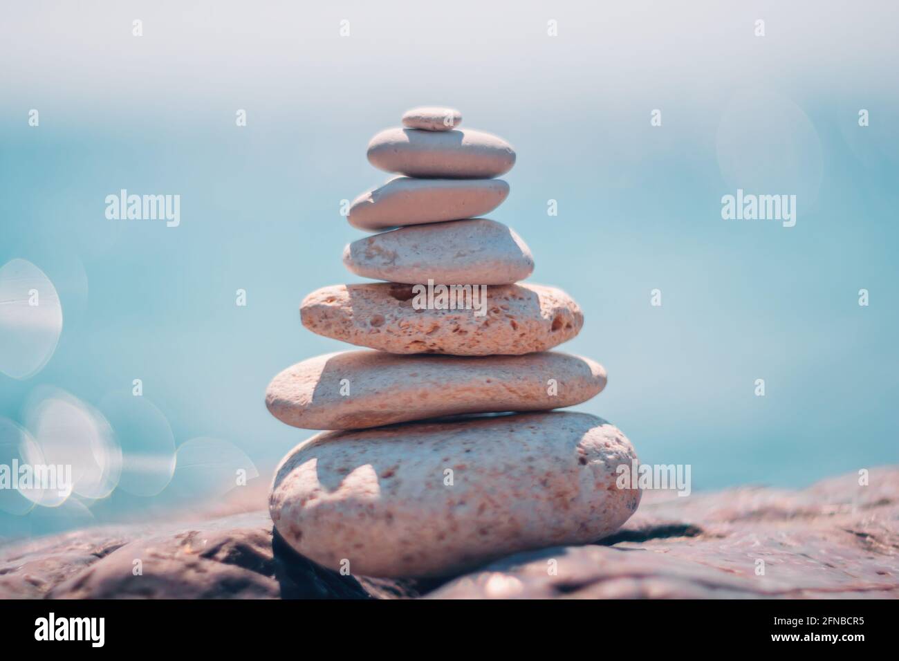Equilibrata piramide di ciottoli sulla spiaggia in una giornata di sole. Abstract Sea bokeh sullo sfondo. Messa a fuoco selettiva. Pietre Zen sulla spiaggia di mare, meditazione Foto Stock