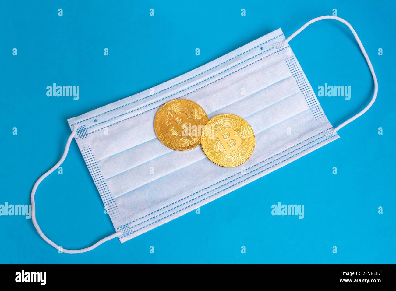 Bitcoins e maschera medica su sfondo blu primo piano Foto Stock