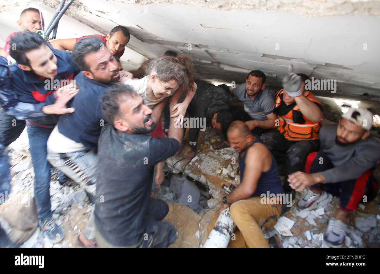 I soccorritori trasportano una ragazza mentre cercano le vittime fra le macerie al luogo degli attacchi aerei israeliani, nella città di Gaza 16 maggio 2021. REUTERS/Mohammed Salem Foto Stock