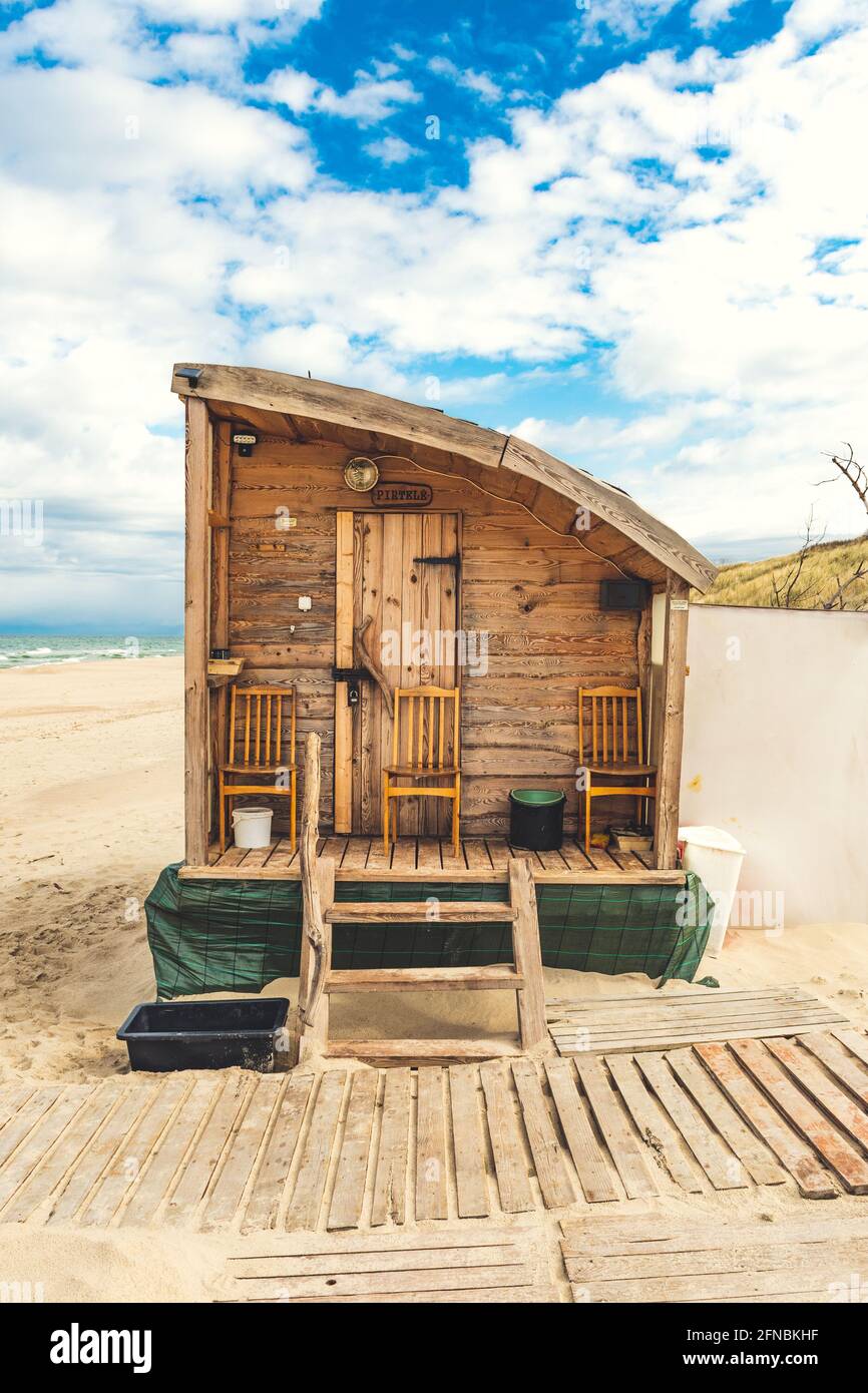 Bella sauna di legno su una spiaggia di sabbia per affittare con mare ruvido e drammatico cielo nuvoloso su sfondo, verticale Foto Stock