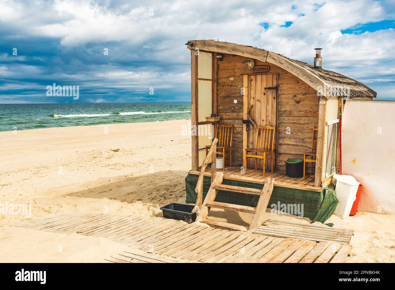 Bella sauna di legno su una spiaggia di sabbia per affittare con mare ruvido e cielo nuvoloso drammatico sullo sfondo Foto Stock
