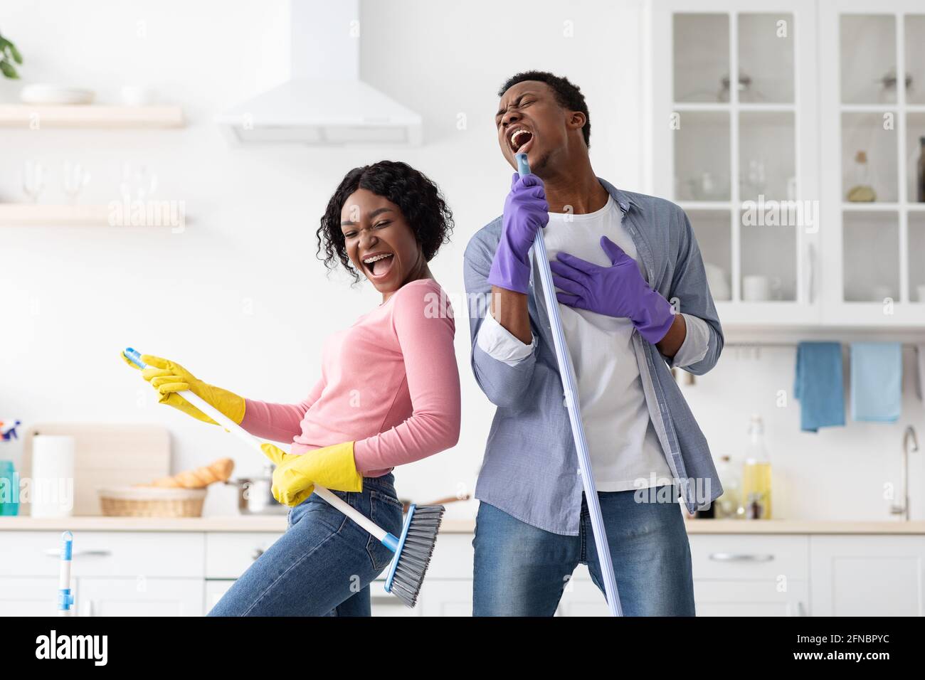 Coppia nera estatica che imita stelle rock durante la pulizia della casa Foto Stock