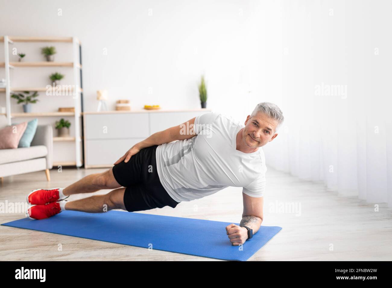 Concetto di stile di vita sano. Fit uomo maturo in piedi nella tavola laterale sul tappeto sportivo a casa, in palestra in soggiorno Foto Stock