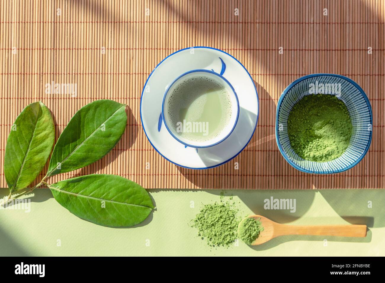 Tè verde matcha in una tazza bianca, tè in polvere e cucchiaio di legno su tovagliolo di bambù, vista dall'alto. Bevanda sana. Disposizione piatta Foto Stock