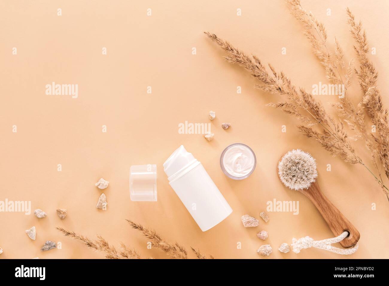 Cosmetici naturali biologici e spazzola in legno per il viso con decorazione in erba secca su sfondo beige. Vista dall'alto, disposizione piatta. Spazio di copia Foto Stock