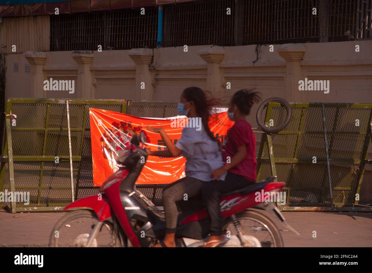 Phnom Penh, Cambogia. 16 maggio 2021. Dopo 4 settimane di chiusura totale della città, il governo continua a dividere Phnom Penh in 3 zone di colore (rosso, arancione e giallo) a causa del continuo aumento COVID - 19. Due giovani donne cambogiane, in maschere facciali protettive e su una moto, Velocità di un blocco stradale in una "zona arancione", il che significa miduim rischio di infezione. Credit: Kraig Lieb/Alamy Live News Foto Stock