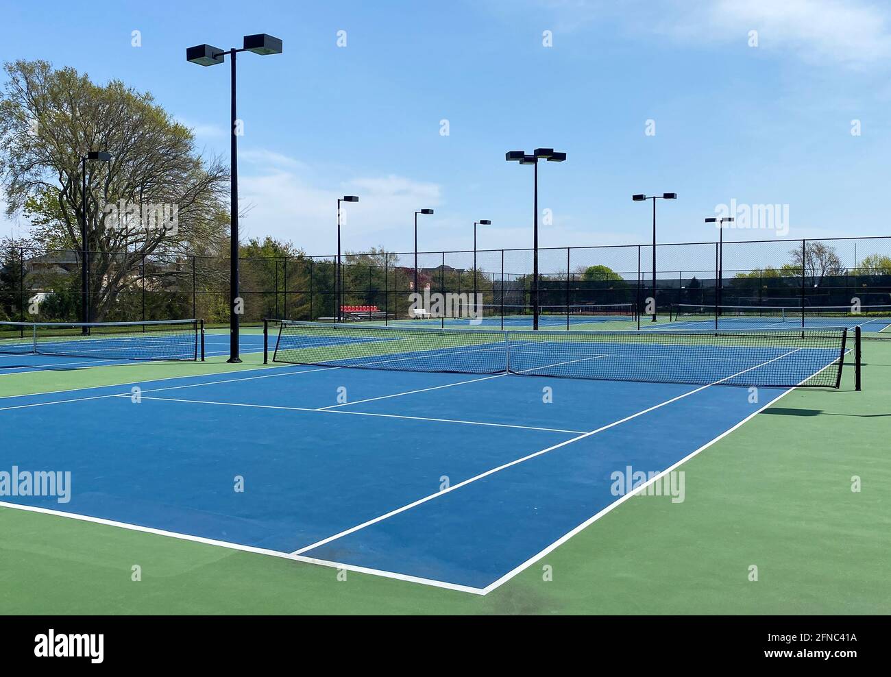Un campo da tennis vuoto con una superficie blu e verde e luci recintate in una scuola locale. Foto Stock