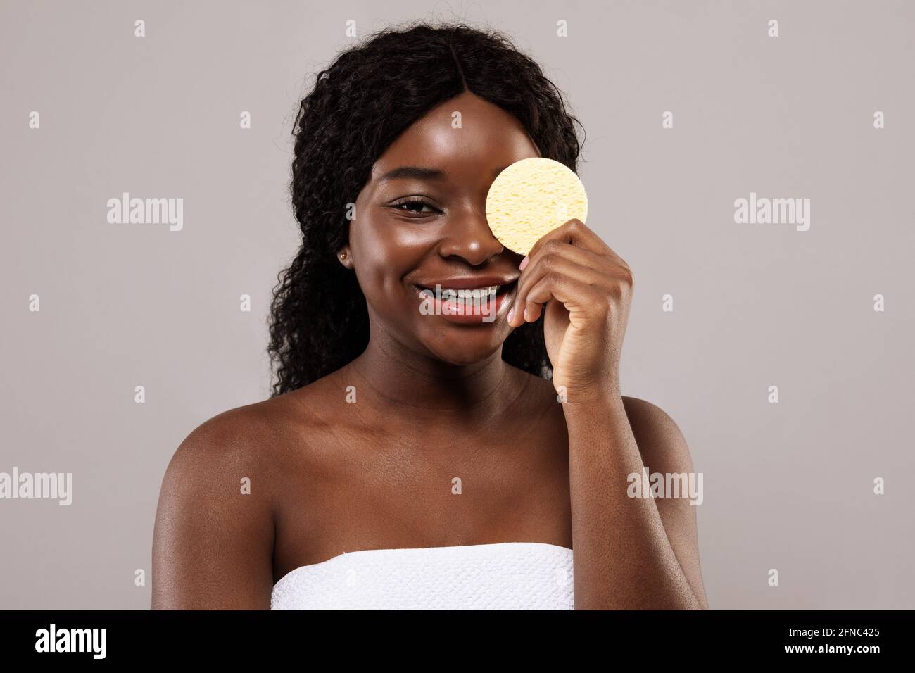 Concetto di cura della pelle. Attraente Black Lady che copre gli occhi con spugna cosmetica Foto Stock