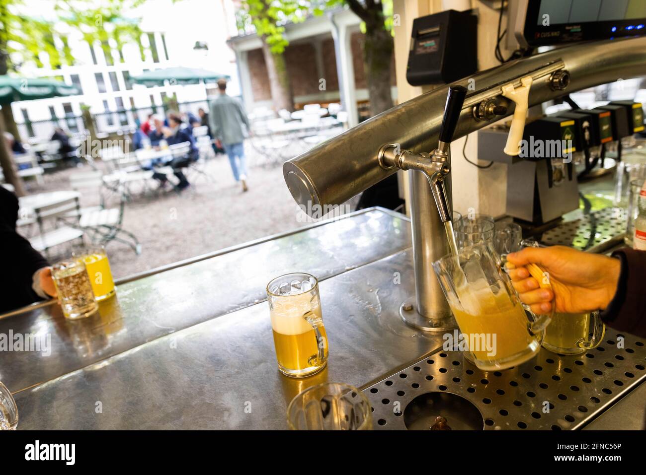 Friburgo, Germania. 16 maggio 2021. Il personale del banco di una birreria all'aperto serve una birra, mentre gli ospiti e il personale della birreria all'aperto possono essere visti sullo sfondo. Alcune regioni del sud-ovest con un'incidenza di più giorni al di sotto di 100 possono ulteriormente rilassare le regole di Corona a partire da questo fine settimana. Credit: Philippe von Ditfurth/dpa/Alamy Live News Foto Stock