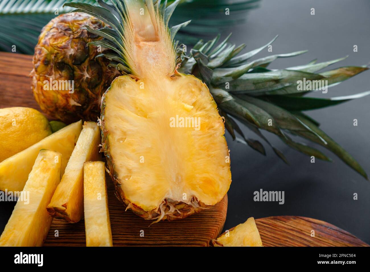 Ananas sul tagliere. Ananas dolce a metà taglio fresco e frutta di ananas intera. Frutta estiva tagliata ananas processo di cottura in cucina al buio Foto Stock