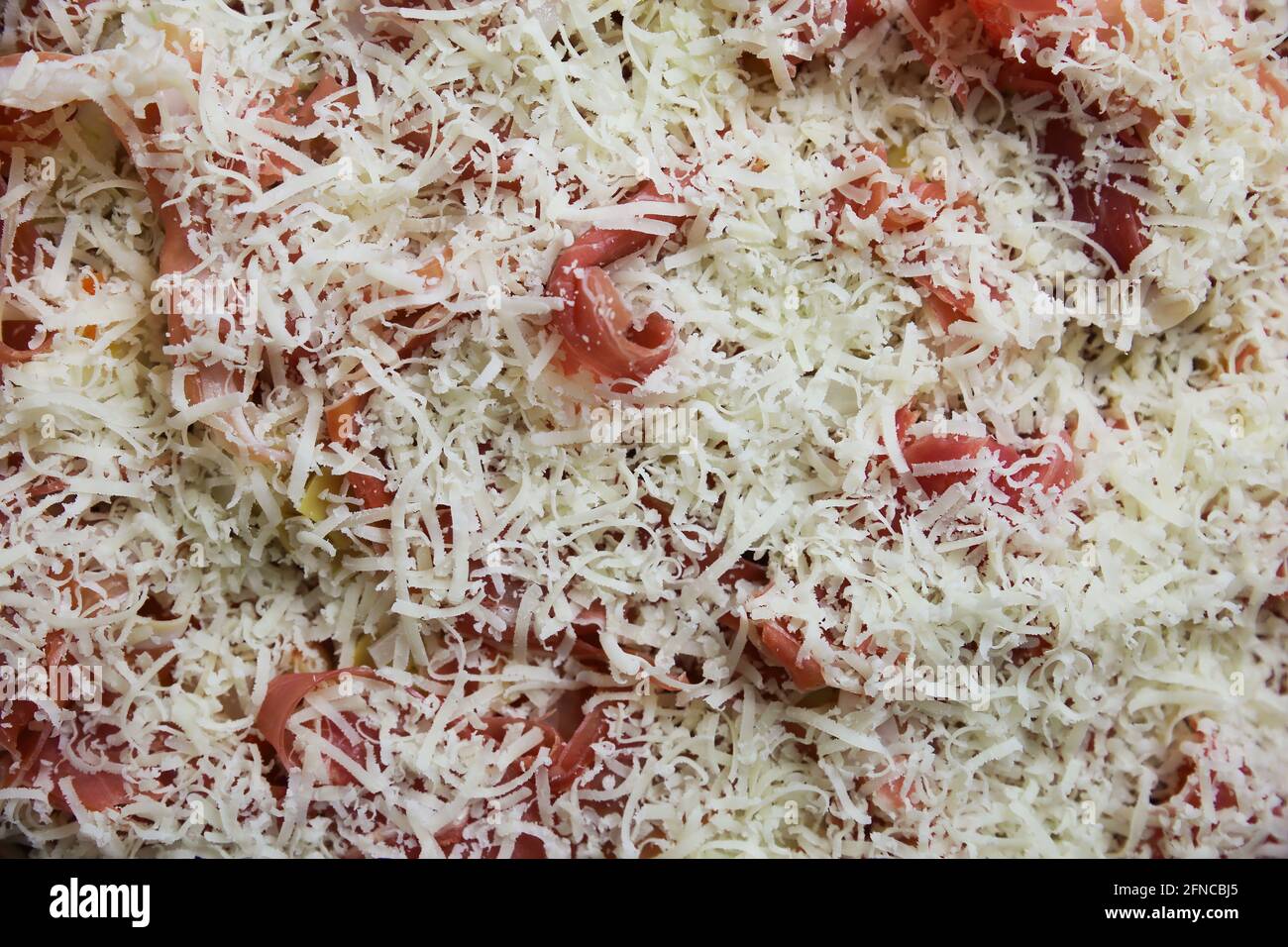 Vista dall'alto su una pizza fresca preparata in casa non cotta isolata con condimenti di base, salsa di pomodoro, prosciutto di serrano e pecorino grattugiato Foto Stock