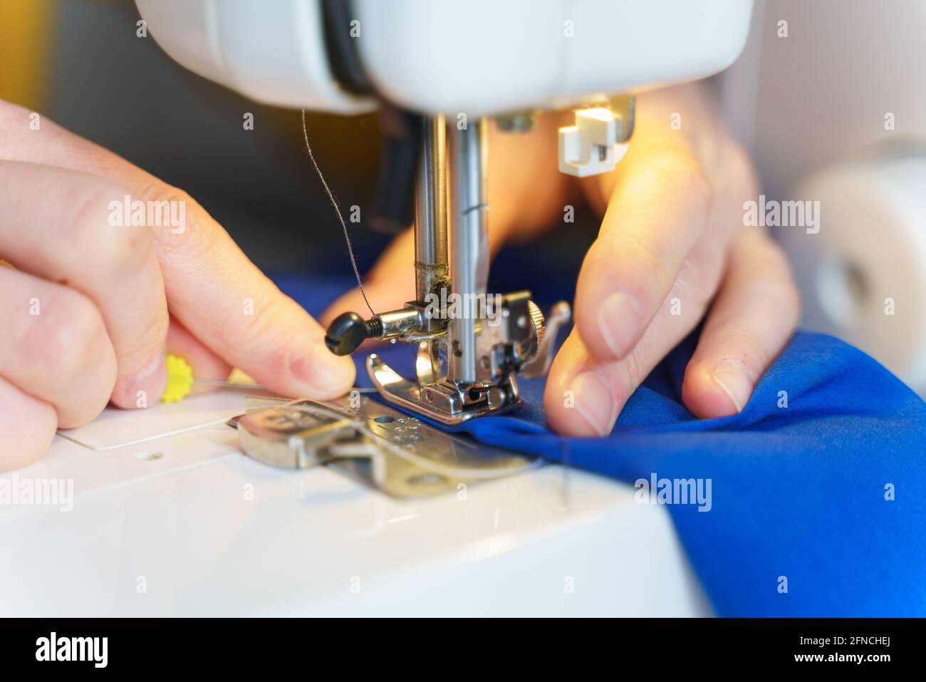 Primo piano di cucire su misura o seamstress o cucire blu navy tessuto con macchina professionale mentre si siede e la creazione di nuovi capi di abbigliamento sul suo posto di lavoro in atelier o officina, fuoco selettivo Foto Stock