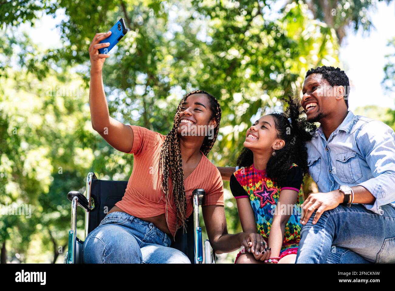 Donna in sedia a rotelle che prende un selfie con la sua famiglia. Foto Stock