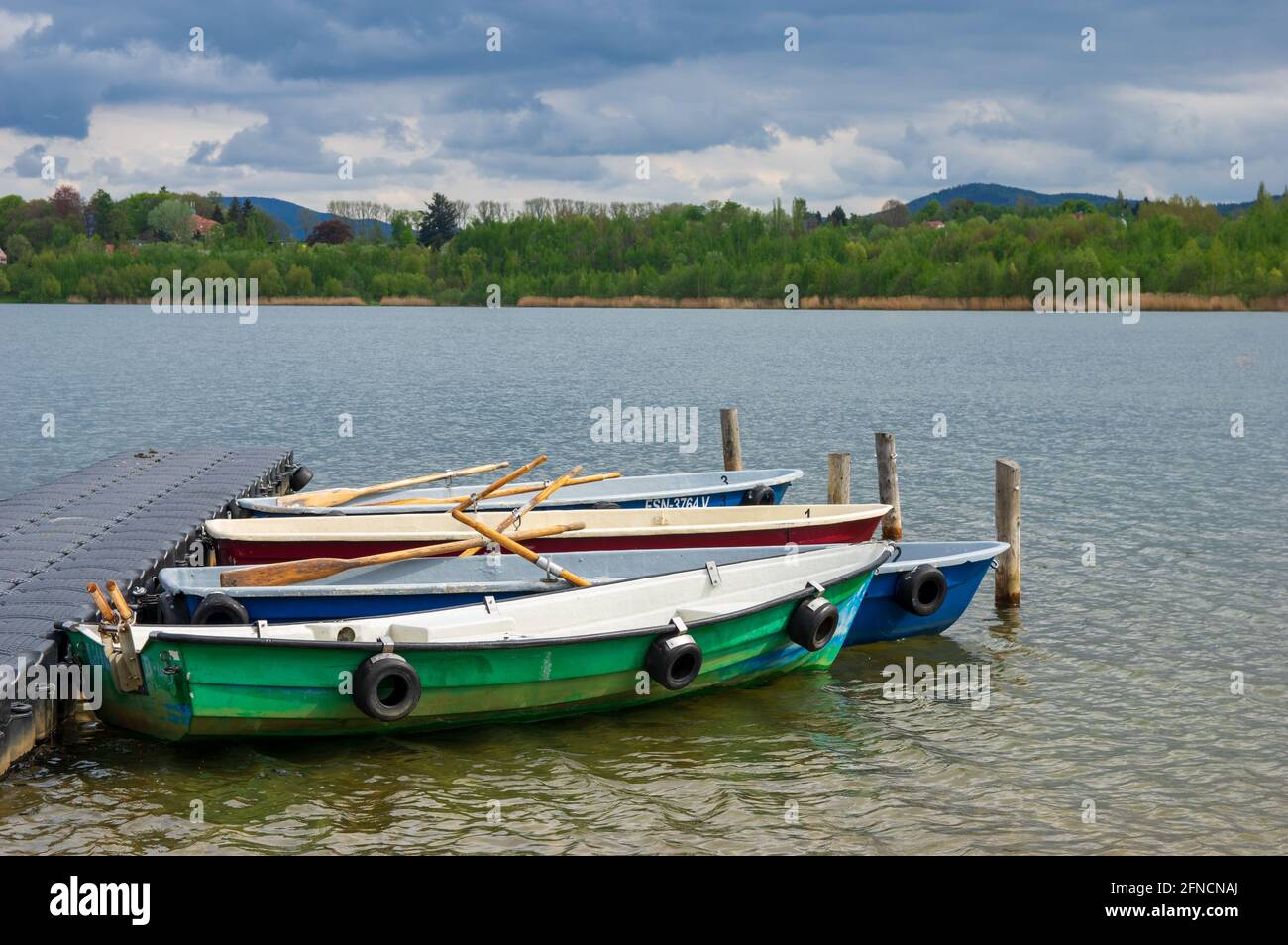 barche ormeggiate a remi su un molo su un lago con vista panoramica sulle montagne e sulle nuvole sullo sfondo Foto Stock