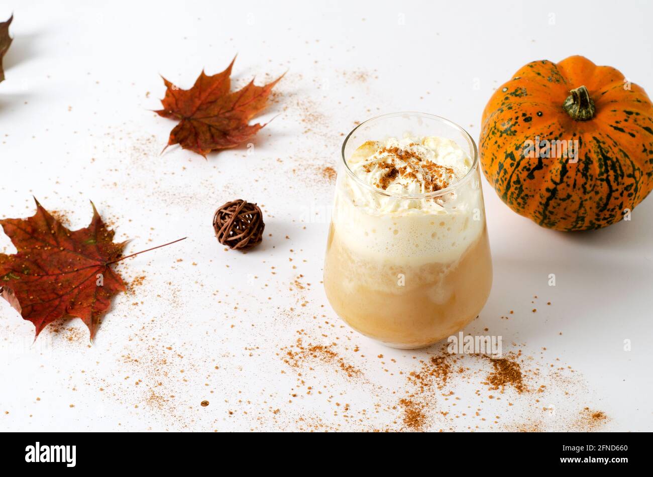 Latte di zucca piccante in un bicchiere con panna e cannella. Concetto di bevanda calda autunnale con zucche e foglie autunnali su sfondo bianco con copia spa Foto Stock