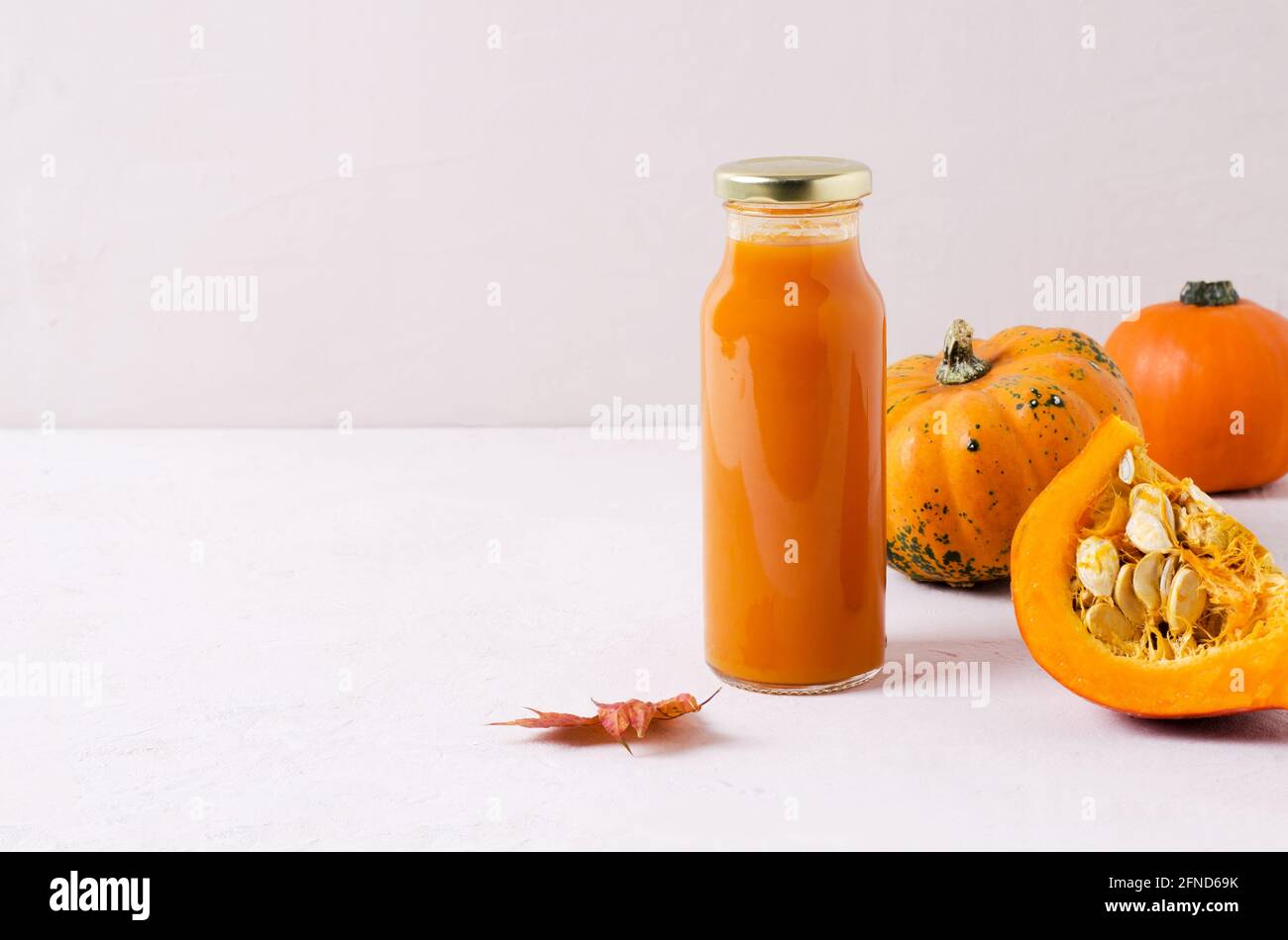 Il succo vegetale utile e dietetico della zucca in una bottiglia di vetro si erge su uno sfondo beige, accanto a una zucca tagliata con semi. Il concetto di a h Foto Stock
