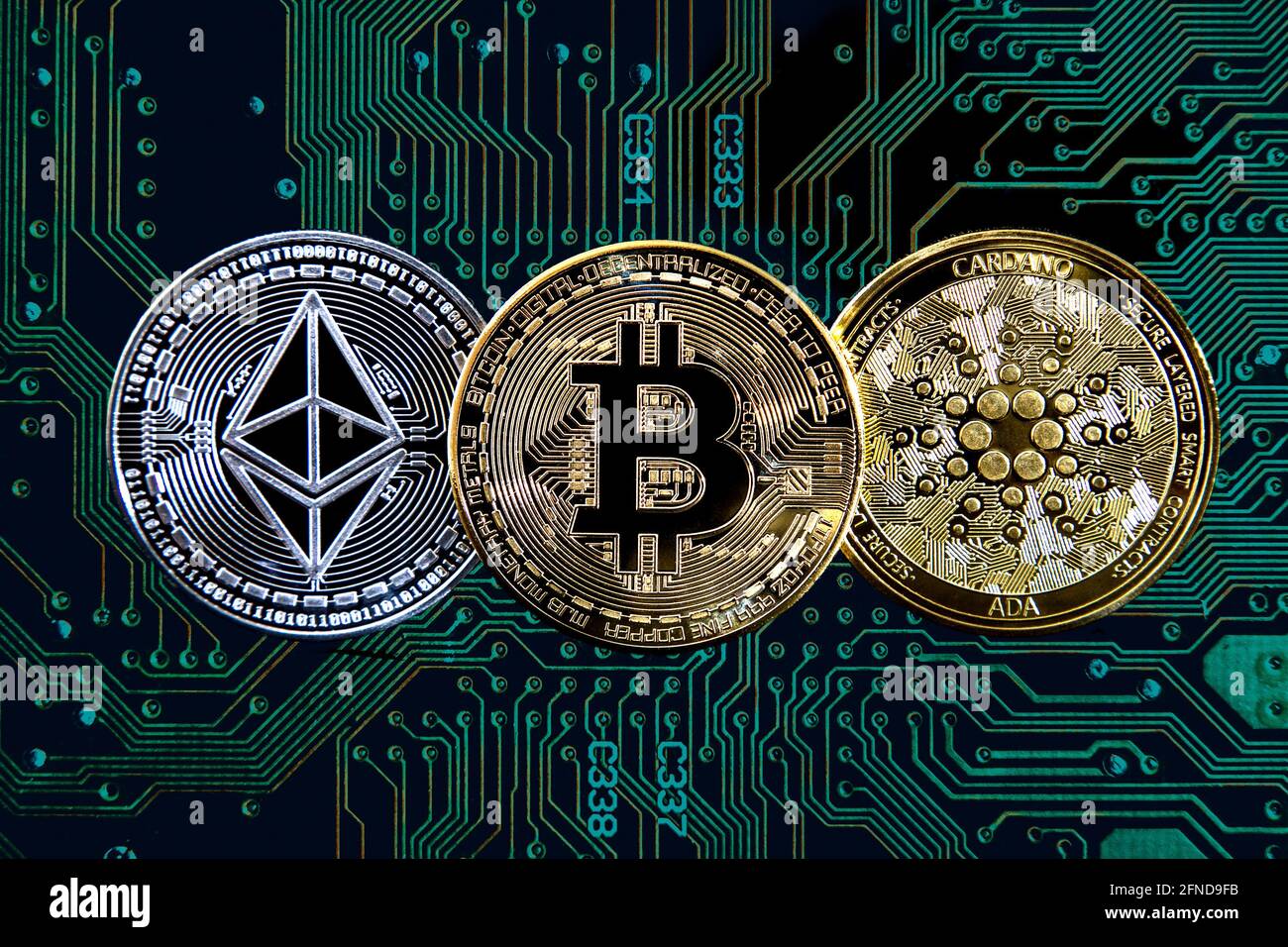 Monete con codice Bitcoin, etereo (etere) e criptovaluta cardano contro lo sfondo della scheda a circuito stampato Foto Stock