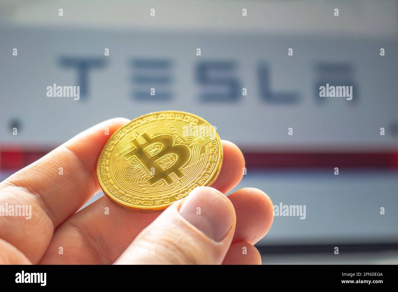 Calgary, Alberta, Canada. 14 maggio 2021. Una persona che tiene una moneta di bit con il logo Tesla sullo sfondo Foto Stock