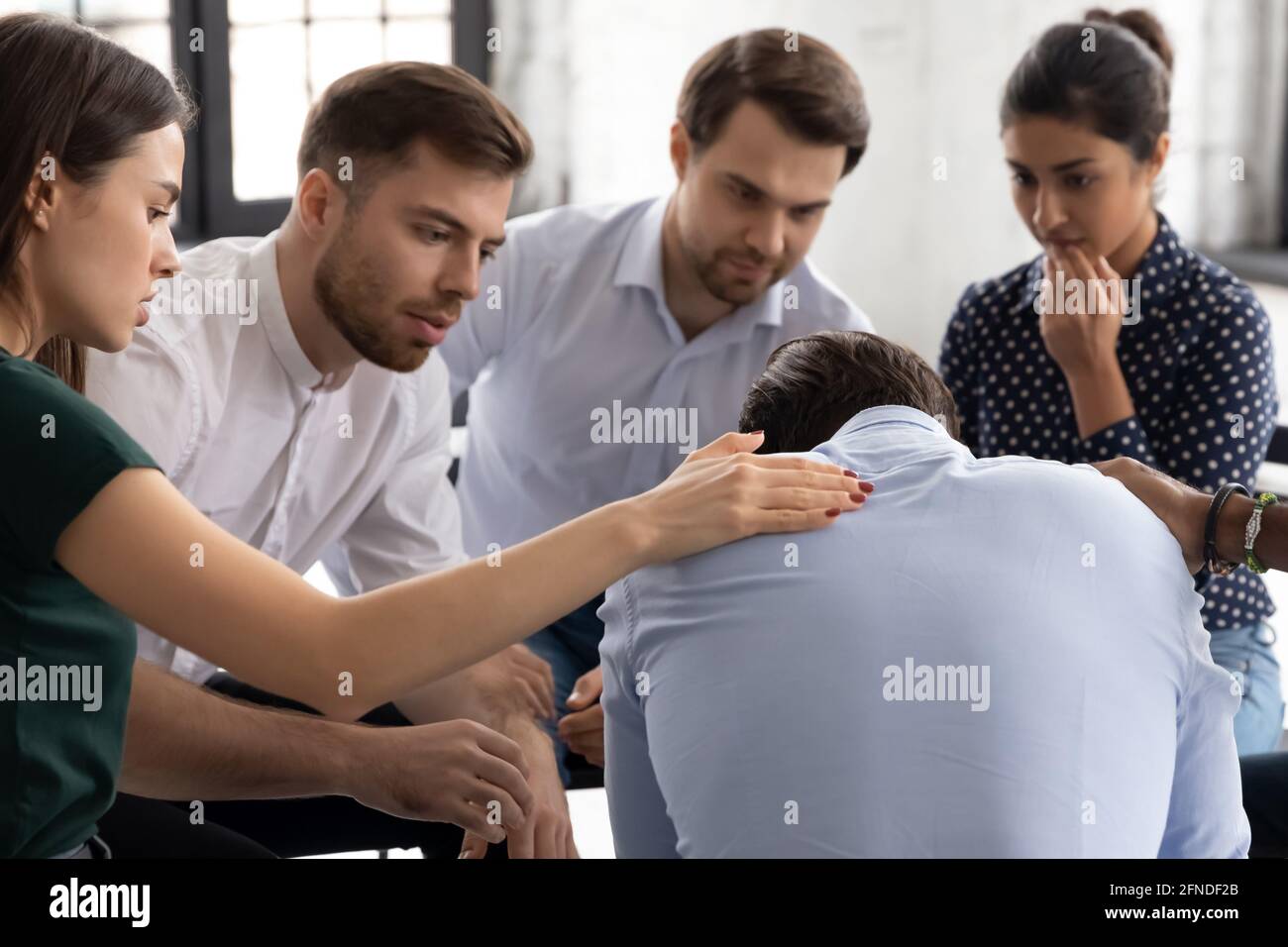 Gruppo diversificato che offre comfort e sostegno a un compagno sconvolto Foto Stock