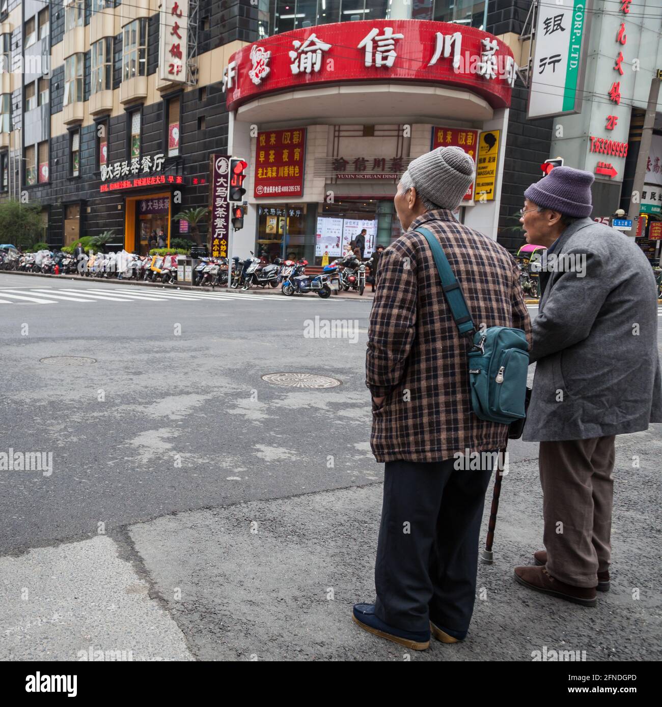 Due anziani signori attendono un semaforo per attraversare un incrocio a Shanghai, Cina Foto Stock