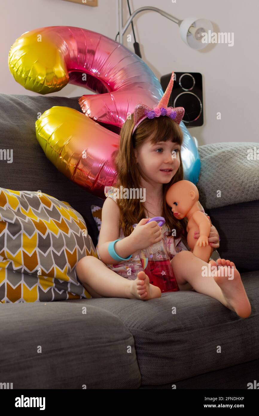 Una ragazza cute del bambino seduta su UN divano con UN Mongolfiera colorata e una bambola Foto Stock