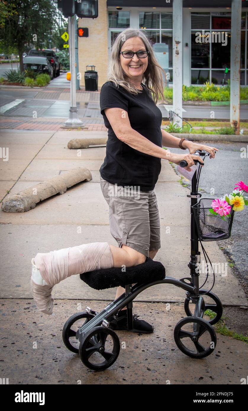 Donna su scooter mobile per strada con gamba avvolti sorridente alla telecamera Foto Stock