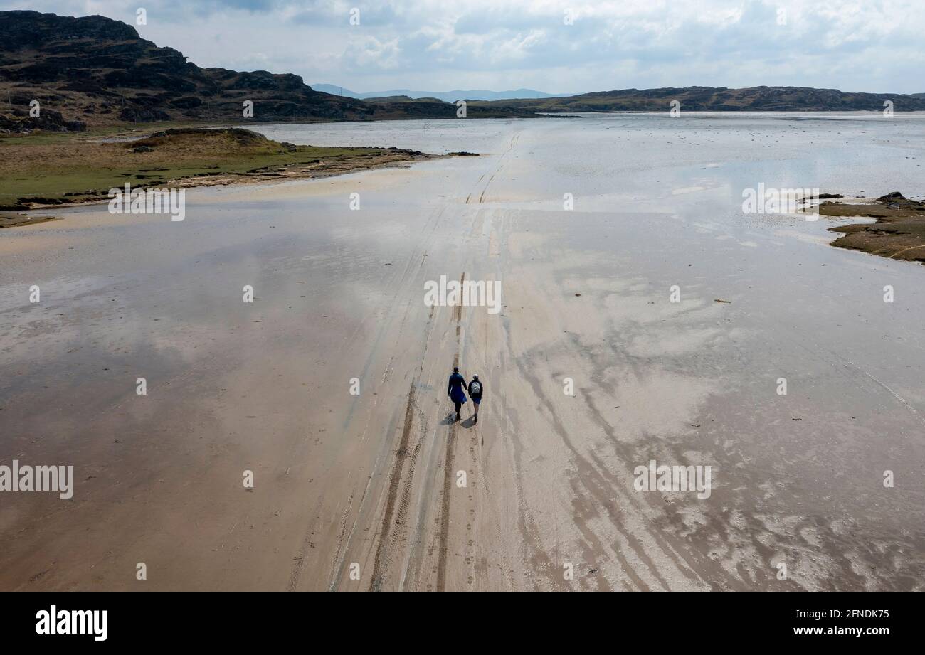 Due escursionisti seguono le tracce di pneumatici nella sabbia che conduce all'isola delle maree di Oronsay, l'isola Strand di Colonsay, Scozia, Regno Unito Foto Stock