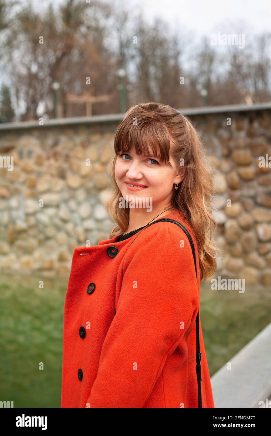 Giovane donna in un cappotto primaverile in un caldo periodo autunnale in un parco cittadino Foto Stock