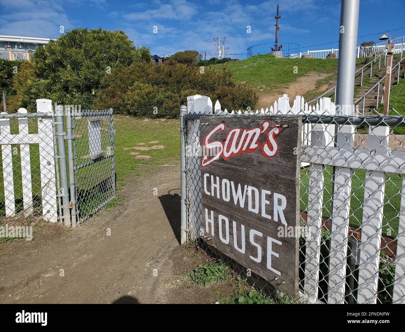 Ripresa angolata di una recinzione con un cartello 'Sam's Chowder House' e un cancello aperto con un sentiero sterrato e scale che conducono a un passaggio costiero e Pillar Point Harbor Beach a Half Moon Bay, California, 30 gennaio 2021. () Foto Stock