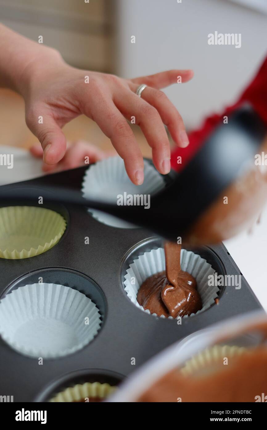 Asian filippino donna aiutare il suo bambino versare salsa di cioccolato in cupcakes a casa a Ottawa, Ontario, Canada Foto Stock