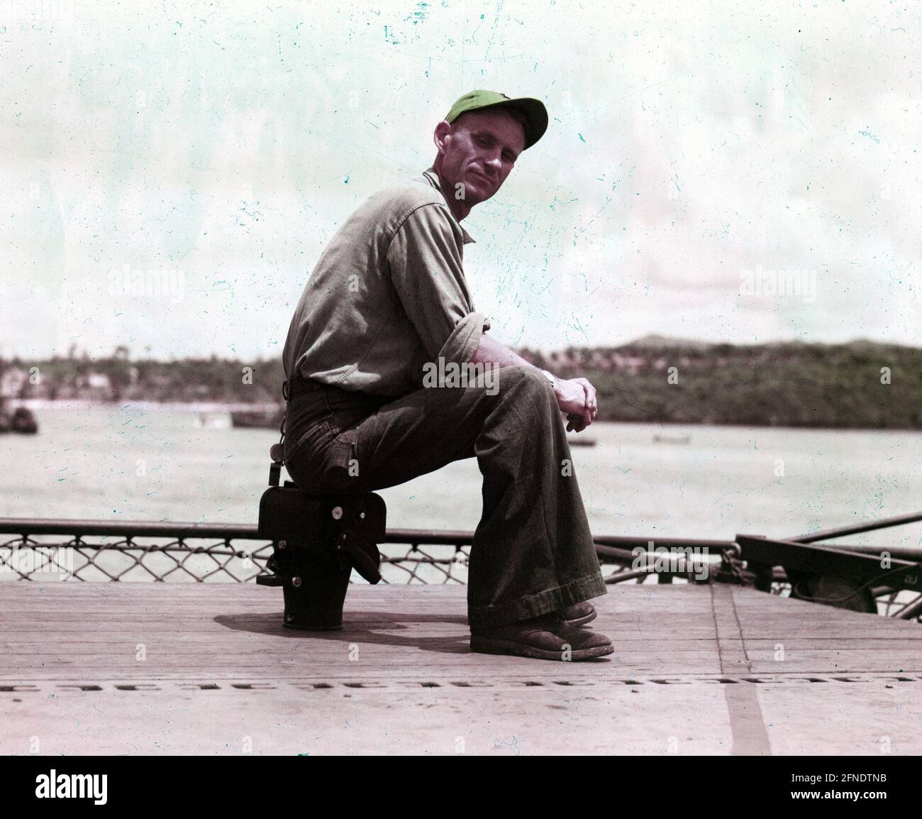 Vera immagine a colori di fotografo su una nave che indossa stanchi di combattimento e utilizzando la sua fotocamera di medio formato come sedile, Filippine, 1945. () Foto Stock