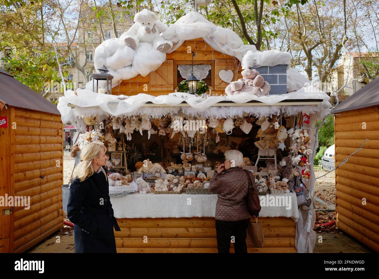 Le decorazioni del mercato di Natale e il venditore di giocattoli imbottiti si trovano a due clienti che fanno acquisti nel centro di Montpellier, Occitanie, nel sud della Francia Foto Stock