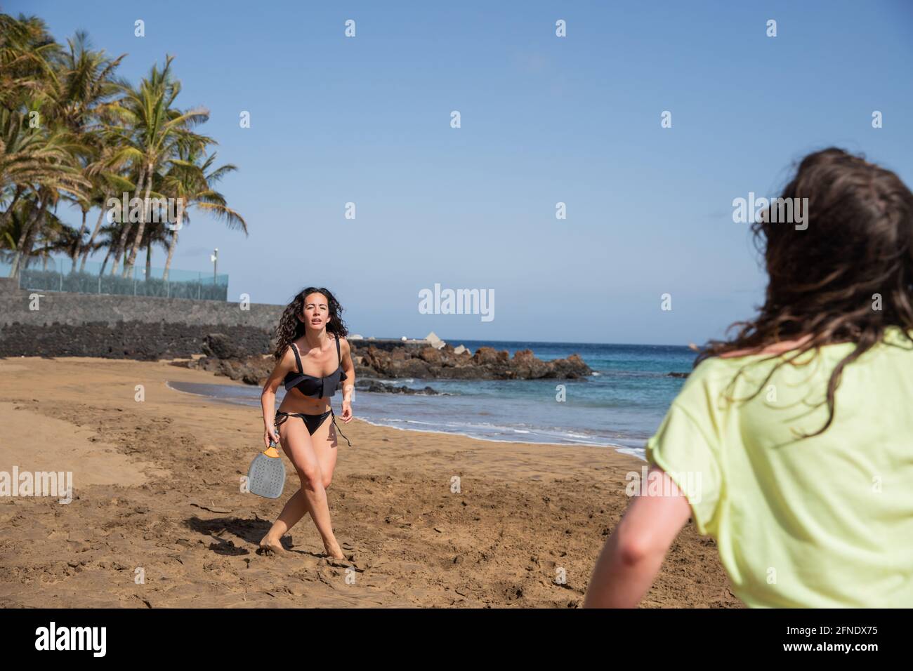 primo piano di una ragazza che gioca a tennis da spiaggia con il suo amico durante la loro vacanza in un luogo esotico Foto Stock