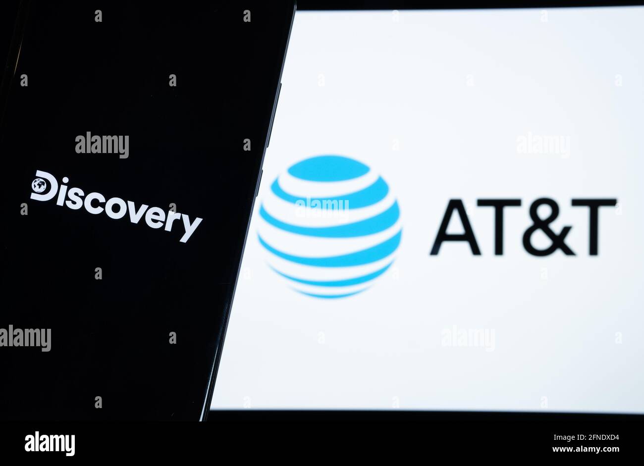Concetto di fusione di Discovery e AT&T. Logo Discovery visualizzato sullo smartphone scuro e LOGO AT&T sullo schermo del notebook sfocato sul retro. Staffor, Re Unito Foto Stock